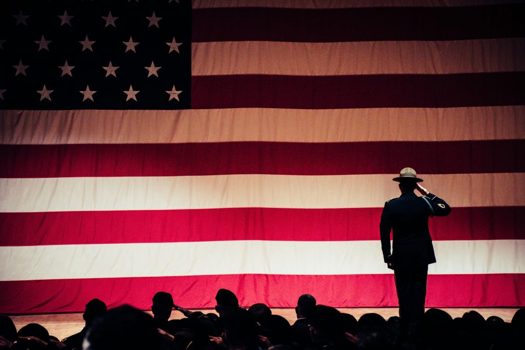 pexels-photo-1340504-1340504 A solemn moment as a soldier salutes the American flag during a ceremony inside an auditorium.